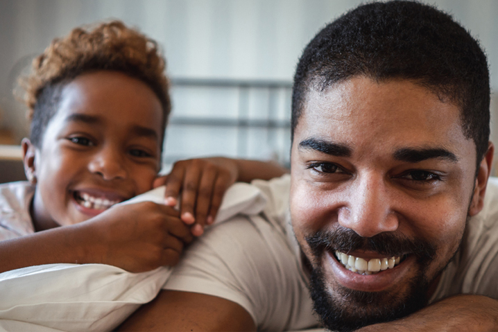 imagem de um pai deitado em uma cama com sua filha sorrindo e olhando para a frente